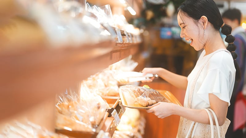 Happy smiling customer asian woman choosing whole grain bread at bakery shop